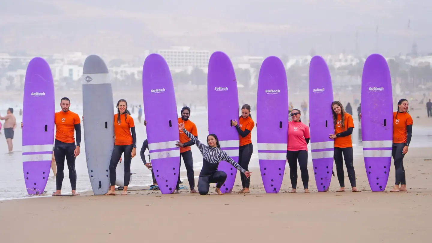 Des surfeurs derrière une rangée de planches en mousse plantées dans le sable